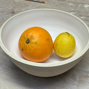 Può includere: Una ciotola di ceramica bianca con un'arancia e un limone al suo interno. La ciotola è su una superficie di legno.