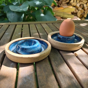 Könnte beinhalten: Zwei blaue und weiße Keramik-Eierbecher. Ein Eierbecher enthält ein braunes Ei. Die Eierbecher stehen auf einer Holzoberfläche.