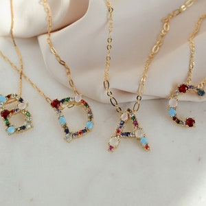 May include: Four gold necklaces with colorful gemstone letter pendants. The letters are A, B, C, and D.
