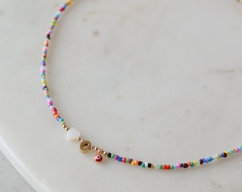 May include: A colourful beaded necklace with a white heart charm and a red and gold evil eye charm.