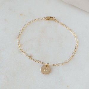 May include: A gold chain bracelet with a small round charm featuring the letter "S" hanging from it.