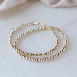 May include: Two gold hoop earrings with a beaded design. The earrings are layered on top of each other.