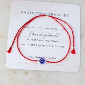 May include: Red string bracelet with a blue evil eye charm. The bracelet is made with 14k gold filled and 925 sterling silver. The card reads "Protection Bracelet" and "Carry with you the protection of this evil eye bracelet to ward off the power and threat of evil eye forces".