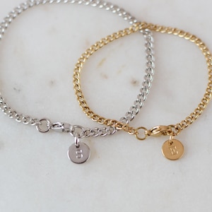 May include: Two curb chain bracelets, one silver-toned and one gold-toned, are displayed. Each bracelet has a small, round charm with a single initial. The silver bracelet has the letter "S", and the gold bracelet has the letter "E".