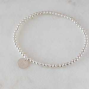 May include: A silver beaded bracelet with a small silver charm. The charm has a design on it.