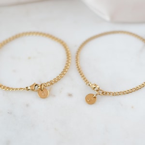 May include: Two gold chain bracelets with small round charms. The charms have a single letter engraved on them.