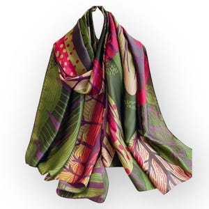 May include: A green, red and purple silk scarf with a floral pattern. The scarf is folded and draped over a white surface.