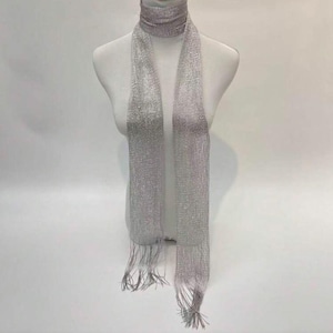 May include: A silver-grey scarf and matching neck wrap, displayed on a mannequin. The scarf is long and rectangular, with a fringed bottom. The fabric appears to be a fine, woven material, possibly with a subtle sheen. The scarf is a neutral colour, suitable for various outfits.