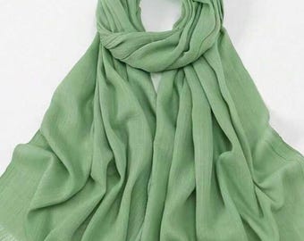 May include: A light green scarf with a fringed edge. The scarf is made of a soft, flowing fabric and is draped in a circular pattern. The scarf is a solid color and is suitable for all seasons.