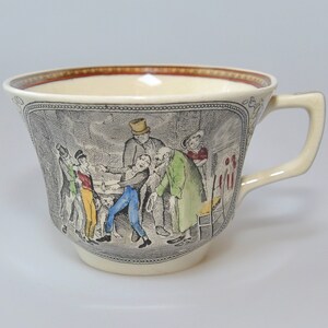 May include: A vintage cream-colored teacup with a brown rim and a black and white illustration of a group of people in a scene. The illustration is in shades of brown, red, blue, and green.