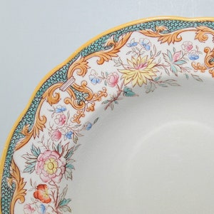 May include: A white ceramic soup bowl with a green and yellow floral design. The bowl has a scalloped edge and a wide rim.