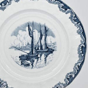 May include: A blue and white porcelain plate with a decorative border and a scene of ships in a harbor. The plate is on a white background.