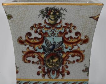 May include: A white ceramic planter with a crackled glaze and a gold rim. The planter features a colourful floral design with a bird and a palm tree.