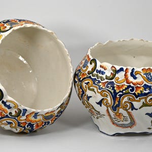May include: Two white ceramic bowls with a scalloped rim. The bowls are decorated with a blue, yellow, and orange floral pattern.