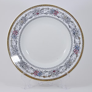 May include: A white ceramic soup bowl with a black and gold floral design. The bowl has a wide rim and a deep well.