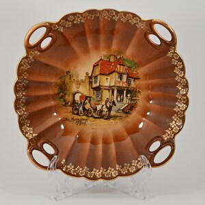 Może przedstawiać: Brązowa ceramiczna miska z pozłacanymi krawędziami i dwoma uchwytami. Miska przedstawia namalowany obraz budynku z czerwonym dachem i powozem konnym. Na misce widnieje napis "The Morre House Oxford".