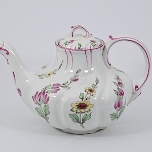Peut inclure: Théière blanche avec un motif floral dans les tons de rose, jaune et vert. La théière a un corps cannelé et un bord rose.