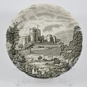 Puede incluir: Un tazón de cerámica blanca con una imagen en blanco y negro de un castillo en un paisaje. El tazón tiene un borde festoneado y está decorado con una imagen en blanco y negro de un castillo, árboles y un río. El castillo está en el centro de la imagen y está rodeado de árboles y un río. El tazón está sobre un fondo blanco.