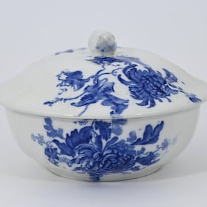 May include: A white ceramic serving bowl with a lid, adorned with blue floral patterns. The bowl has a rounded shape with a lid featuring a small, decorative knob. The blue floral design is consistent across the bowl and lid.