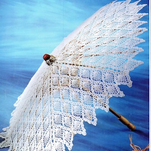 以下が含まれることがあります： 木製の柄と赤い飾り付きの白いかぎ針編みの日傘。繊細なレースのデザインが青い背景に広がり、繊細な職人技を披露しています。この日傘はヴィンテージ風アクセサリーです。