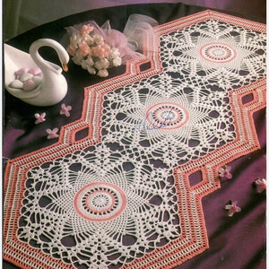 Puede incluir: Un camino de mesa de crochet blanco con un borde rosa y tres doilies hexagonales. Los doilies tienen un diseño delicado y de encaje con un centro rosa.