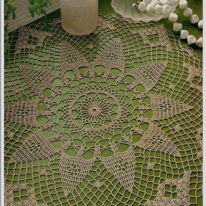 May include: A beige crocheted doily with a circular design and a delicate lace pattern. The doily is laid out on a green surface.