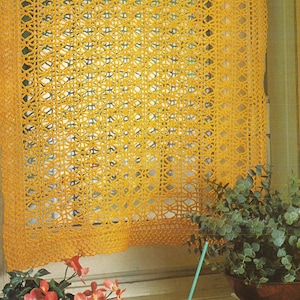 May include: A yellow crocheted curtain with a geometric pattern hangs in a window. The curtain is made of a fine yarn and has a delicate, lacy look.