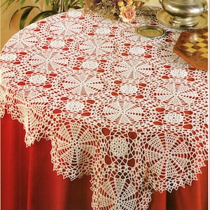 May include: White crocheted tablecloth with a delicate floral pattern. The tablecloth is laid on a red table and features a circular design with intricate details.