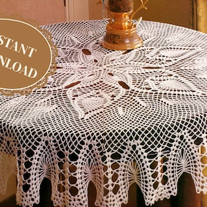 Pode incluir: Uma toalha de mesa redonda de crochê branco com um padrão floral detalhado cobre uma mesa de madeira escura. A toalha de mesa tem uma borda ondulada e um design decorativo. As palavras "INSTANT DOWNLOAD" são impressas em um círculo marrom.