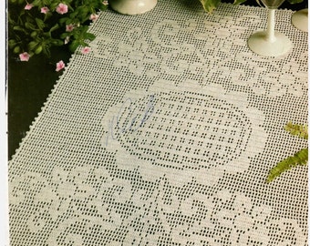 May include: A white crocheted table runner with three floral designs. The runner is on a dark surface with a plate of pink and white meringue cookies and a glass of wine.