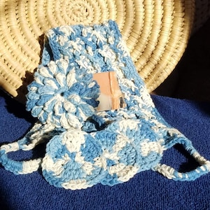 May include: A blue and white variegated crochet exfoliating strap featuring a circular flower-shaped scrubber attached to the main body, accompanied by a rectangular bar of peach and white soap nestled within the textured, hand-stitched fabric.