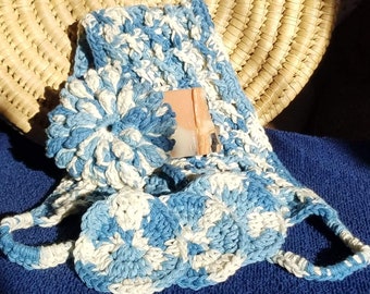 May include: A blue and white variegated crochet exfoliating strap featuring a circular flower-shaped scrubber attached to the main body, accompanied by a rectangular bar of peach and white soap nestled within the textured, hand-stitched fabric.