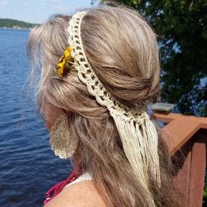 May include: A crocheted headband with a long fringe and a small yellow flower accent. The headband is worn by a person with long, light brown hair.