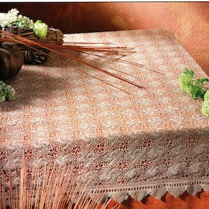 May include: A white crocheted tablecloth with a delicate floral pattern. The tablecloth is laid on a brown table and has a scalloped edge.