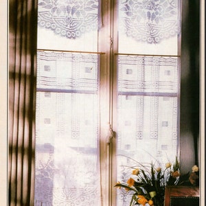 Puede incluir: Cortinas blancas de ganchillo con un diseño floral cuelgan en una ventana con cortinas marrones a cada lado. Un ramo de flores amarillas se encuentra sobre una mesa frente a la ventana.