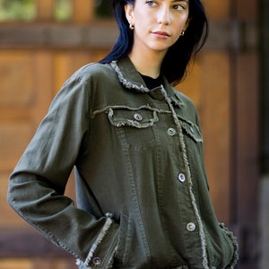 May include: A woman wearing a dark green denim jacket with frayed edges and a black shirt. The jacket has a button closure and pockets.