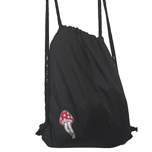 May include: Black drawstring backpack with a red and white mushroom patch. The bag has black rope straps and a cinched top. The mushroom patch features a red cap with white spots and a white stem.