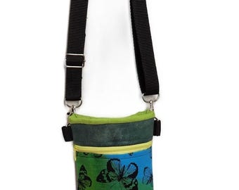 May include: A small, rectangular crossbody bag with a black adjustable strap. The bag features a colorful butterfly print on a gradient background of green, blue, and yellow. It has a zippered pocket and a green top.