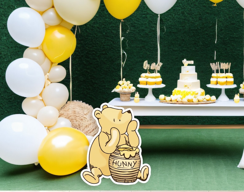 May include: A Winnie the Pooh themed baby shower with a white table decorated with yellow and white balloons, cupcakes, and a cake. A Winnie the Pooh character holding a honey pot with the word "Hunny" on it is in the foreground.