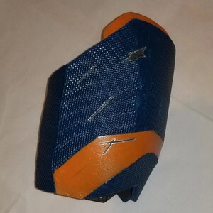 May include: A blue and orange protective arm guard with a textured surface.