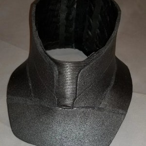 May include: A grey, textured, fabric collar with a ribbed design in the centre. The collar is made of a soft, flexible material and has a slightly curved shape.