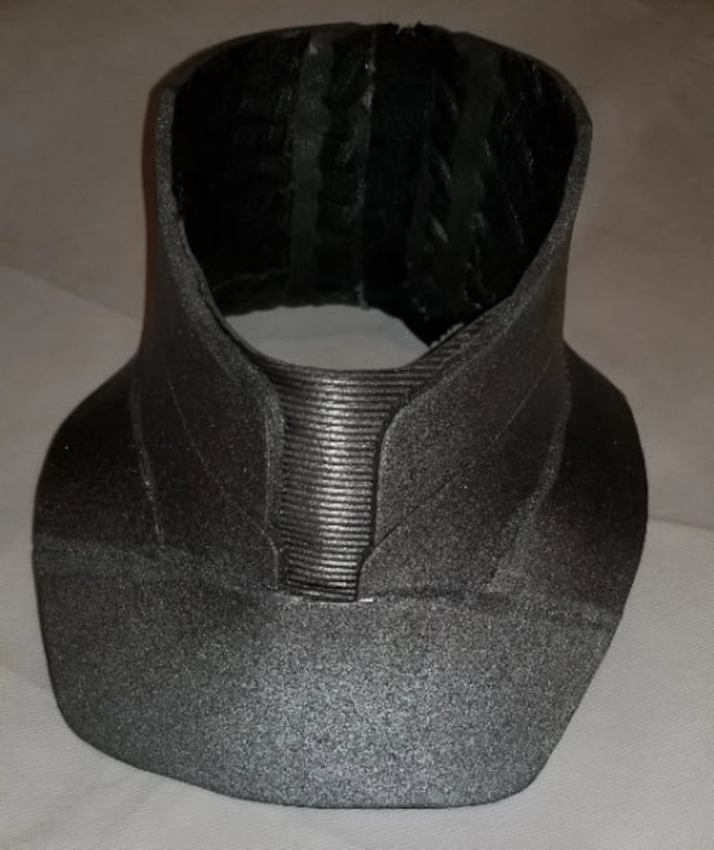 May include: A grey, textured, fabric collar with a ribbed design in the centre. The collar is made of a soft, flexible material and has a slightly curved shape.