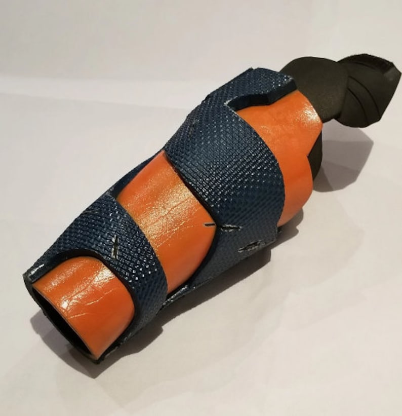 May include: A blue and orange foam arm guard with a black foam piece on the top. The guard has a textured surface and is designed to protect the arm.