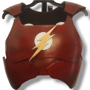 Könnte beinhalten: Rotes und goldenes Superhelden-Kostüm-Bruststück mit einem Blitz-Emblem. Das Bruststück ist aus einem steifen Material gefertigt und hat eine strukturierte Oberfläche.