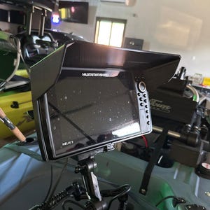 May include: A black Humminbird HELIX 9 fish finder with a sunshade mounted on a kayak. The fish finder has a black and white screen and a variety of buttons.