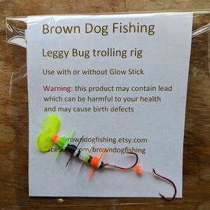 May include: A fishing lure called a "Leggy Bug trolling rig" with a yellow, orange, black, and white body. The lure is packaged on a white card with the text "Brown Dog Fishing" and a warning that the product may contain lead.