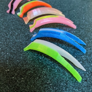 May include: A set of eight colorful plastic finger guards, each with a different color and design. The guards are arranged in a row, with the pink guard at the top and the green guard at the bottom.