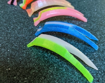 May include: A set of eight colorful plastic finger guards, each with a different color and design. The guards are arranged in a row, with the pink guard at the top and the green guard at the bottom.