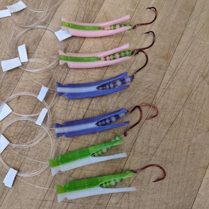 May include: Five fishing lures with different colored bodies and green and white accents. Each lure has a red hook.