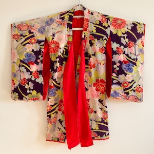 May include: A traditional Japanese kimono with a floral pattern in shades of red, pink, white, and yellow on a dark purple background. The kimono has a red sash and is tied at the front.